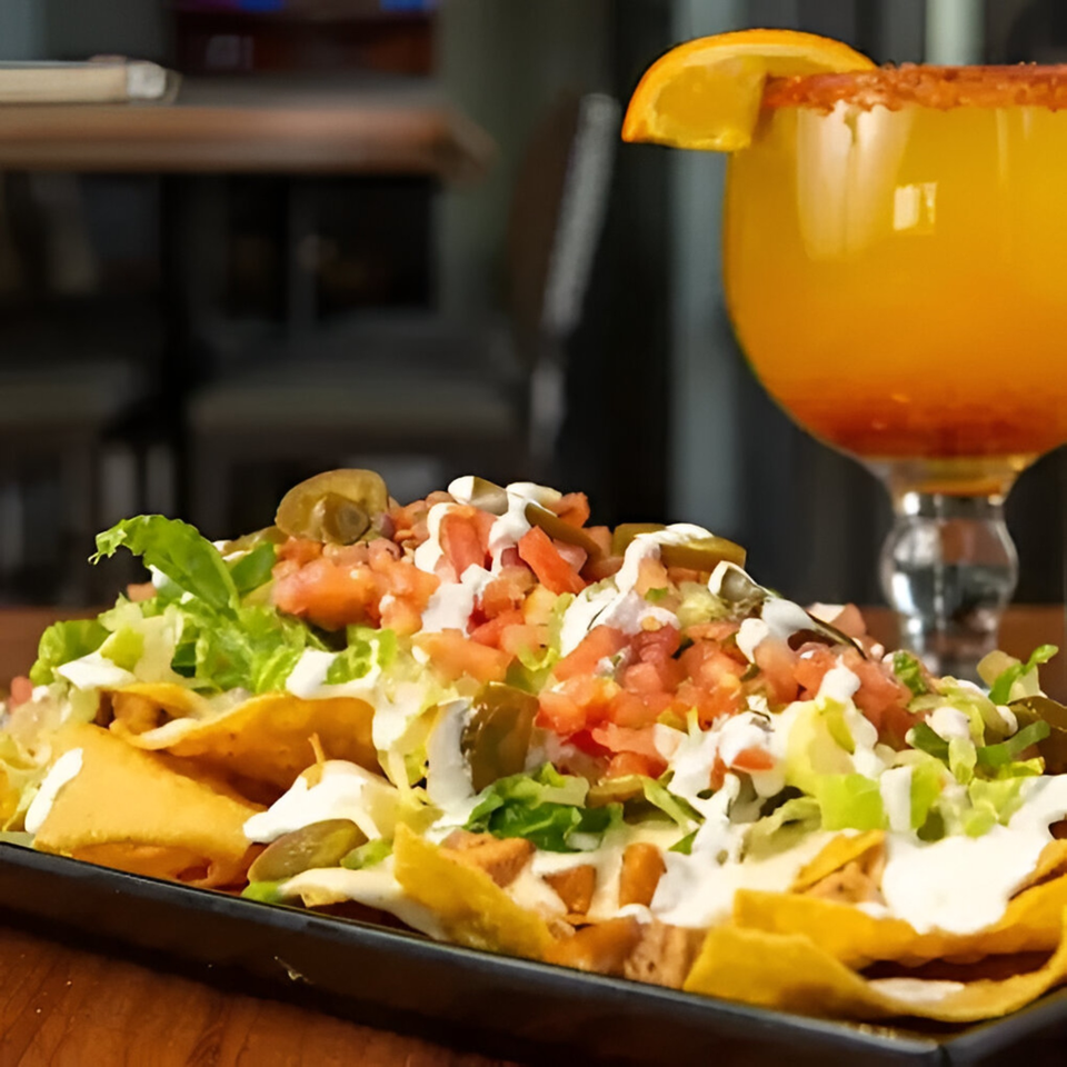 A plate of Habaneros Fresh Mexican Grill nachos with a margarita in the background.