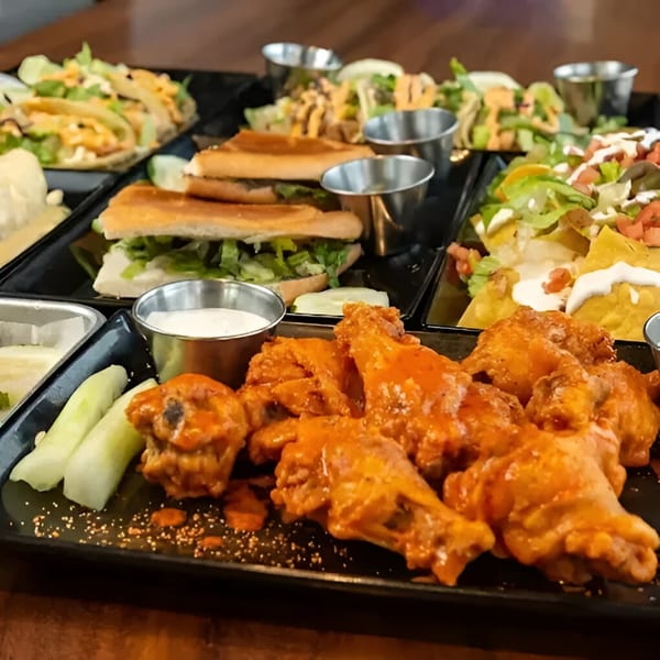 A black tray filled with Habaneros Fresh Mexican Grill's tacos, nachos, sandwiches, and buffalo wings.