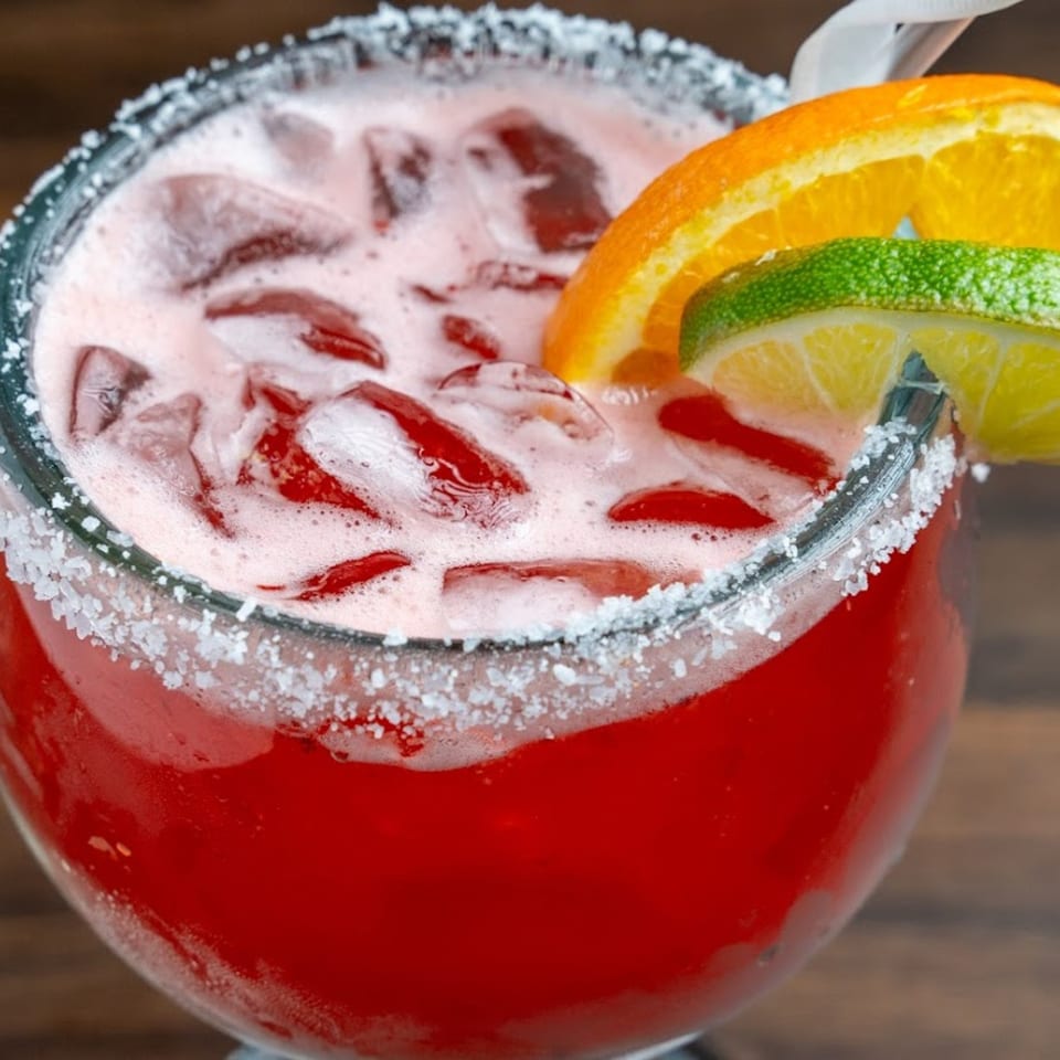 A vibrant red Habaneros Fresh Mexican Grill margarita, garnished with orange and lime slices, and a salted rim.